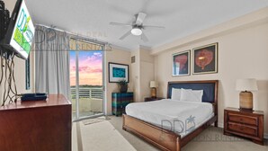 Une chambre d’hôtel équipée d’un lit, d’un bureau, d’une télévision, d’un ventilateur de plafond, d’une fenêtre avec des rideaux et d’œuvres d’art accrochées aux murs.