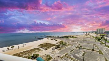 A coastal property with a beach, parking area, and a view of the sea and city skyline.