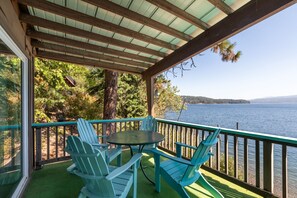 A covered outdoor area with a table and chairs, overlooking a lake and surrounded by trees. - Mica Bay Serenity Cabin w/ Dock, Canoe (Coeur d'Alene)