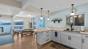 Une cuisine moderne dotée d’un grand îlot central, de meubles blancs et offrant une vue sur l’eau.