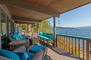 A covered deck with wicker furniture and teal cushions, overlooking a lake with a wooden railing.