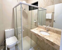 Un baño moderno con ducha de vidrio, inodoro blanco y lavamanos de mármol con un espejo grande.
