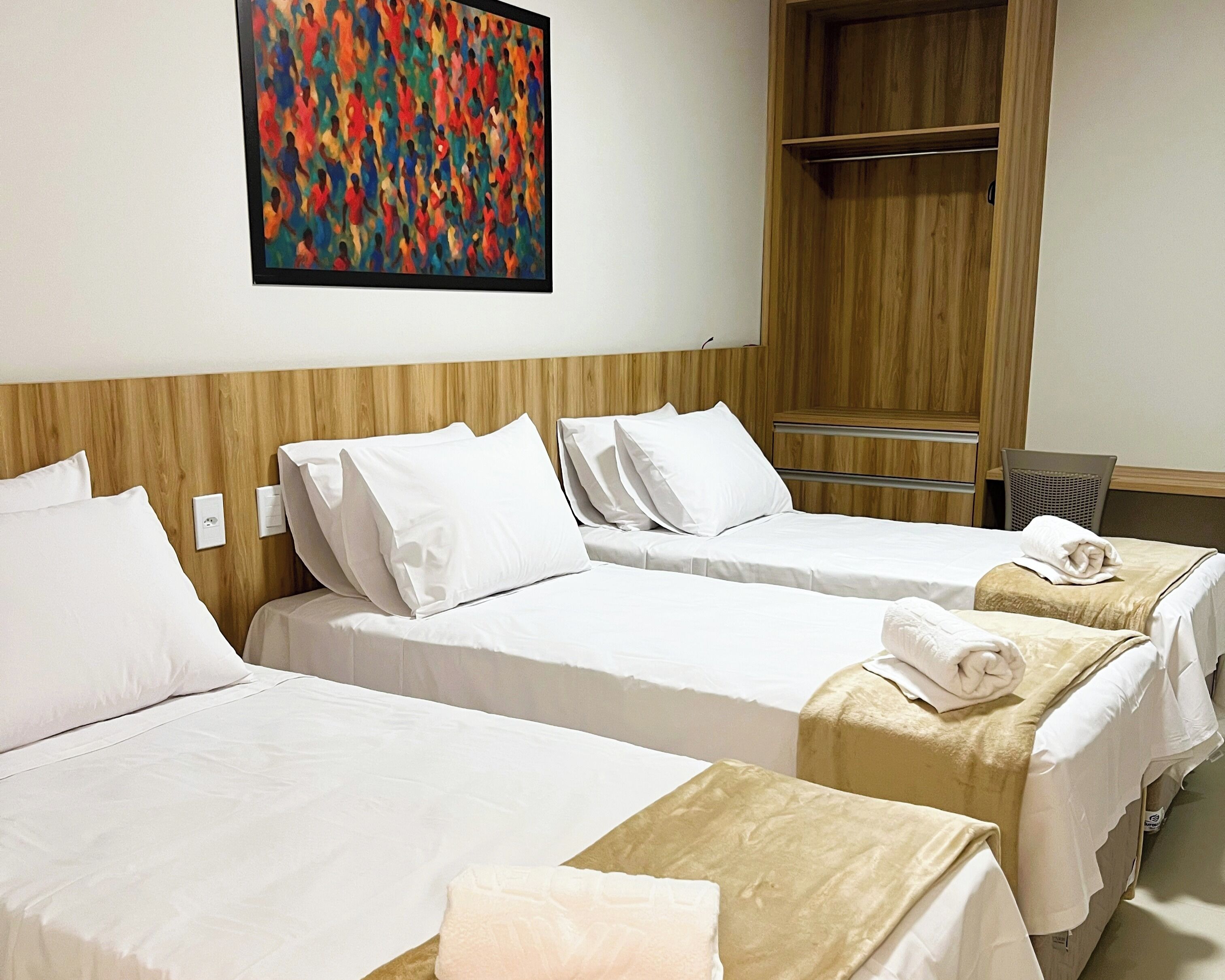 Une chambre d’hôtel avec deux lits simples, une tête de lit en bois, une peinture abstraite aux couleurs vives et une armoire en bois.