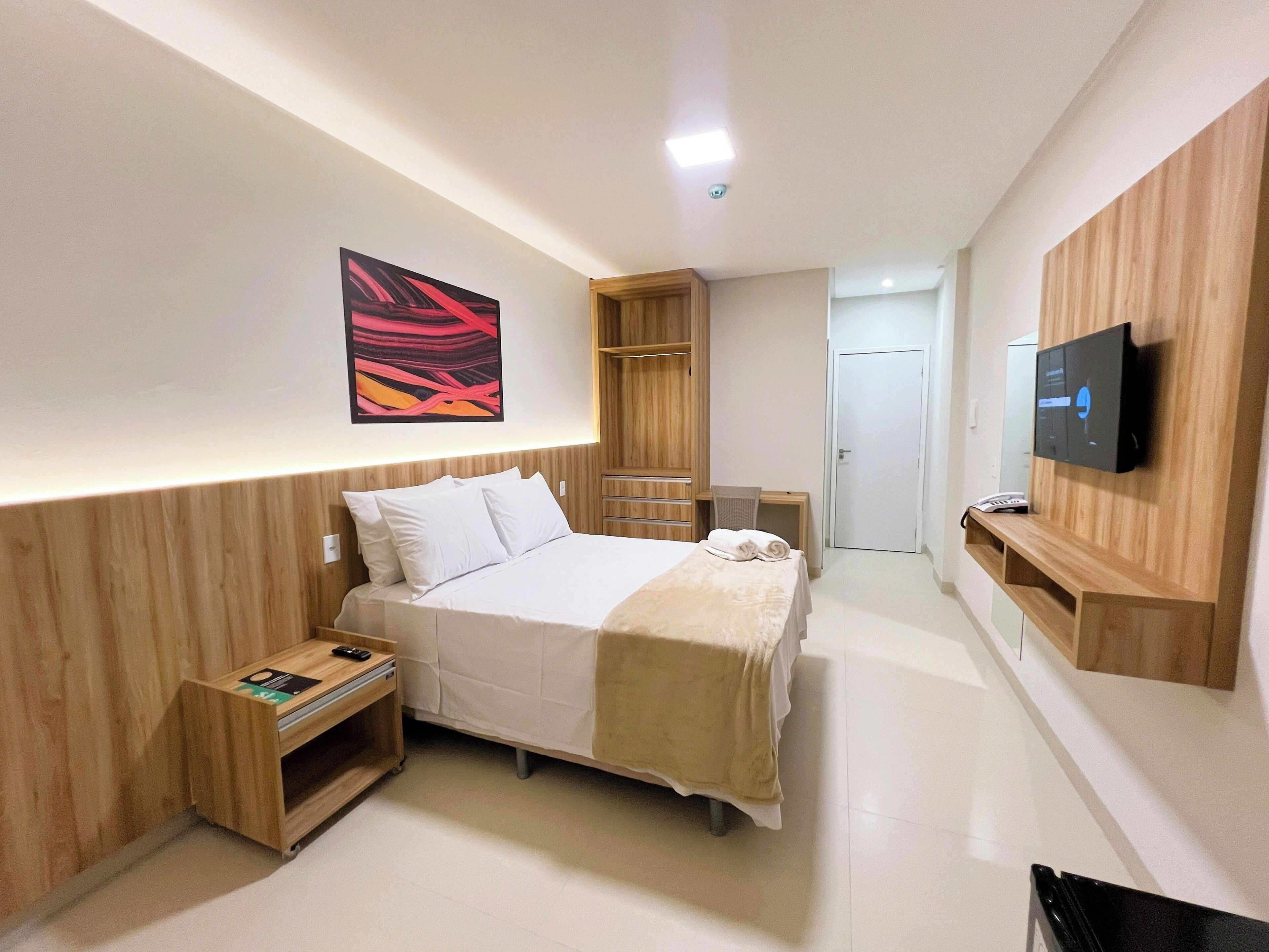 Una habitación de hotel moderna con cama, televisor, escritorio y armario.