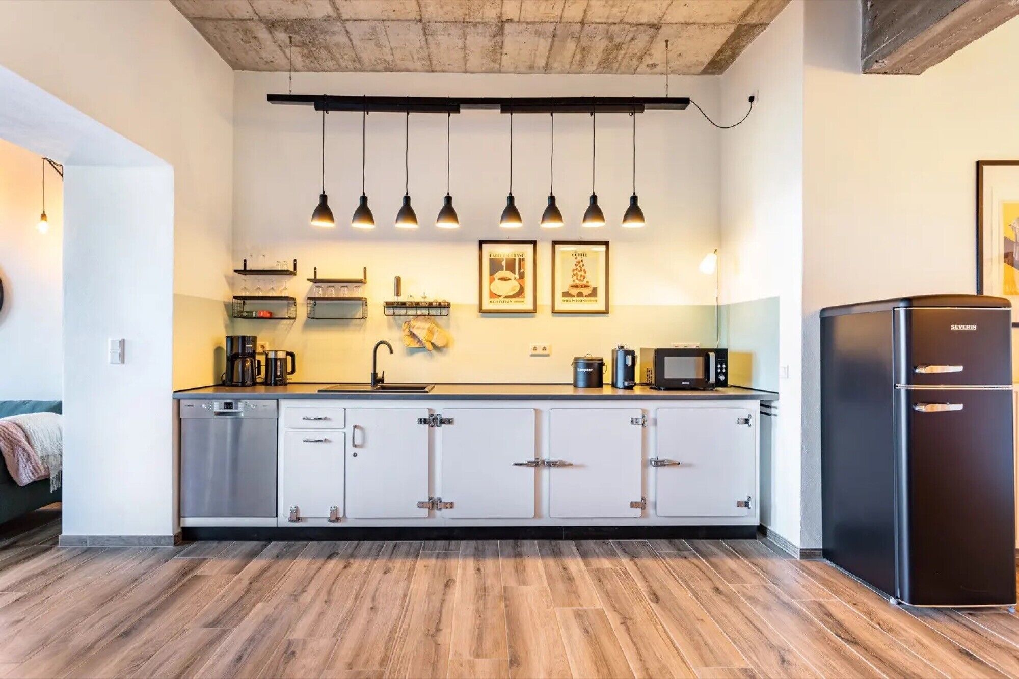 Een moderne keuken met een centraal eiland, inbouwapparatuur, hangende lampen en een koelkast.