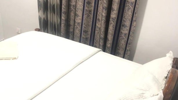A bed with a white sheet and a wooden headboard. - Immaculate 10-bed Lodge in Kigali (Kigali)