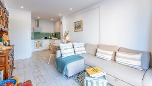 Een moderne woonkamer met een bank, een eethoek met een tafel, en een keuken op de achtergrond.