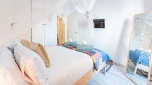 Een slaapkamer met een bed, nachtkastje, spiegel en televisie aan de muur.