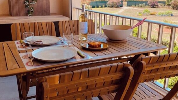 A wooden dining table with plates, glasses, and a bowl on a balcony overlooking a scenic view. - Apartment for rent - Cap d'Agde, plage Richelieu Sea view - Quiet - Comfort - (CAP D'AGDE)