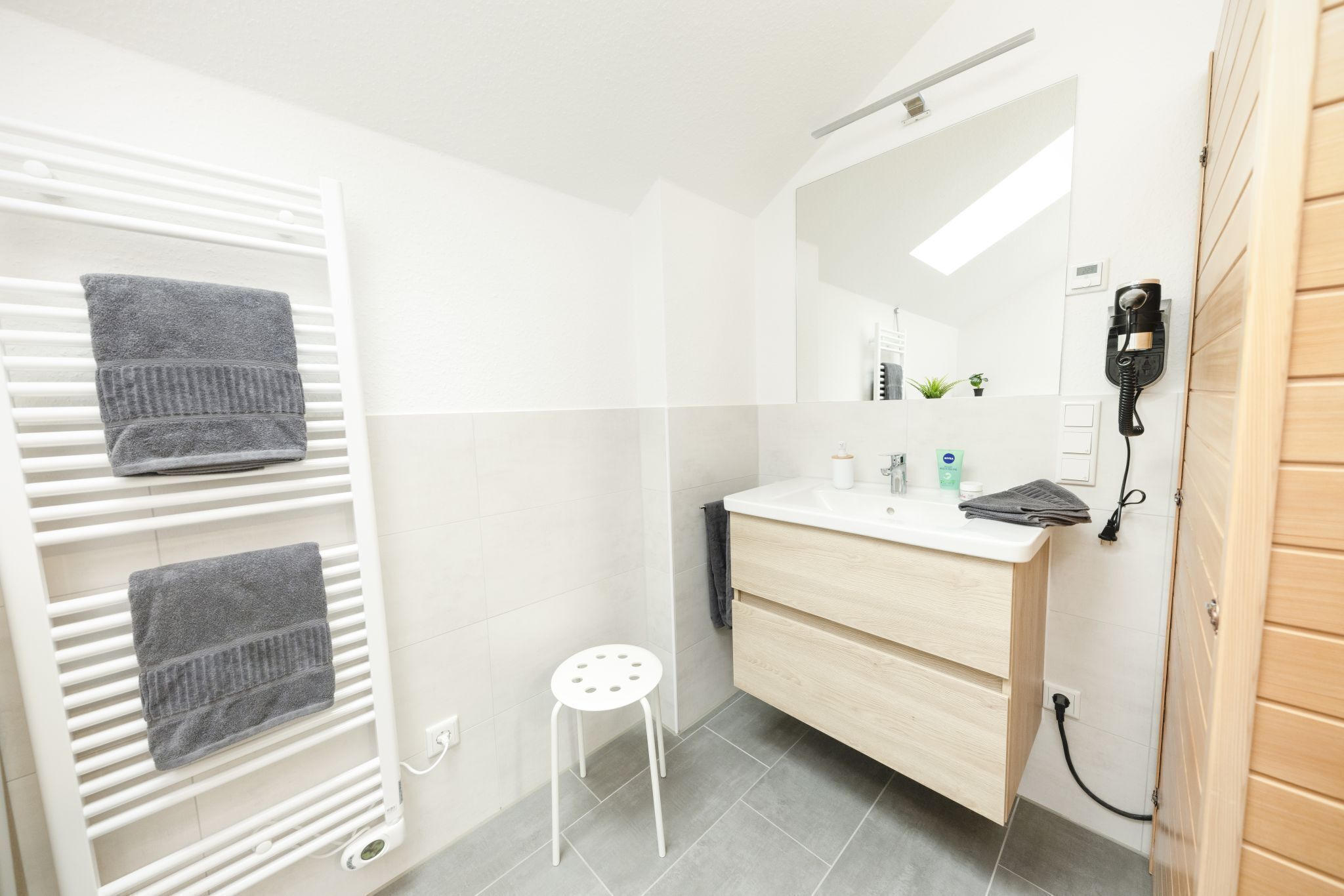A modern bathroom with a white towel rack, a small stool, a wooden vanity, and a mirror.