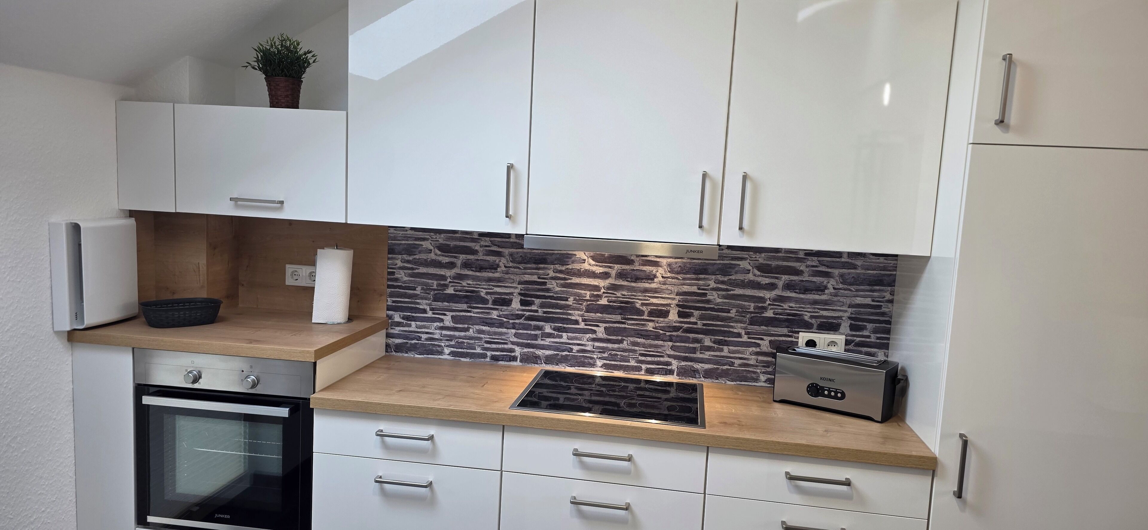 A modern kitchen with white cabinets, a stone backsplash, a built-in oven, and a toaster.