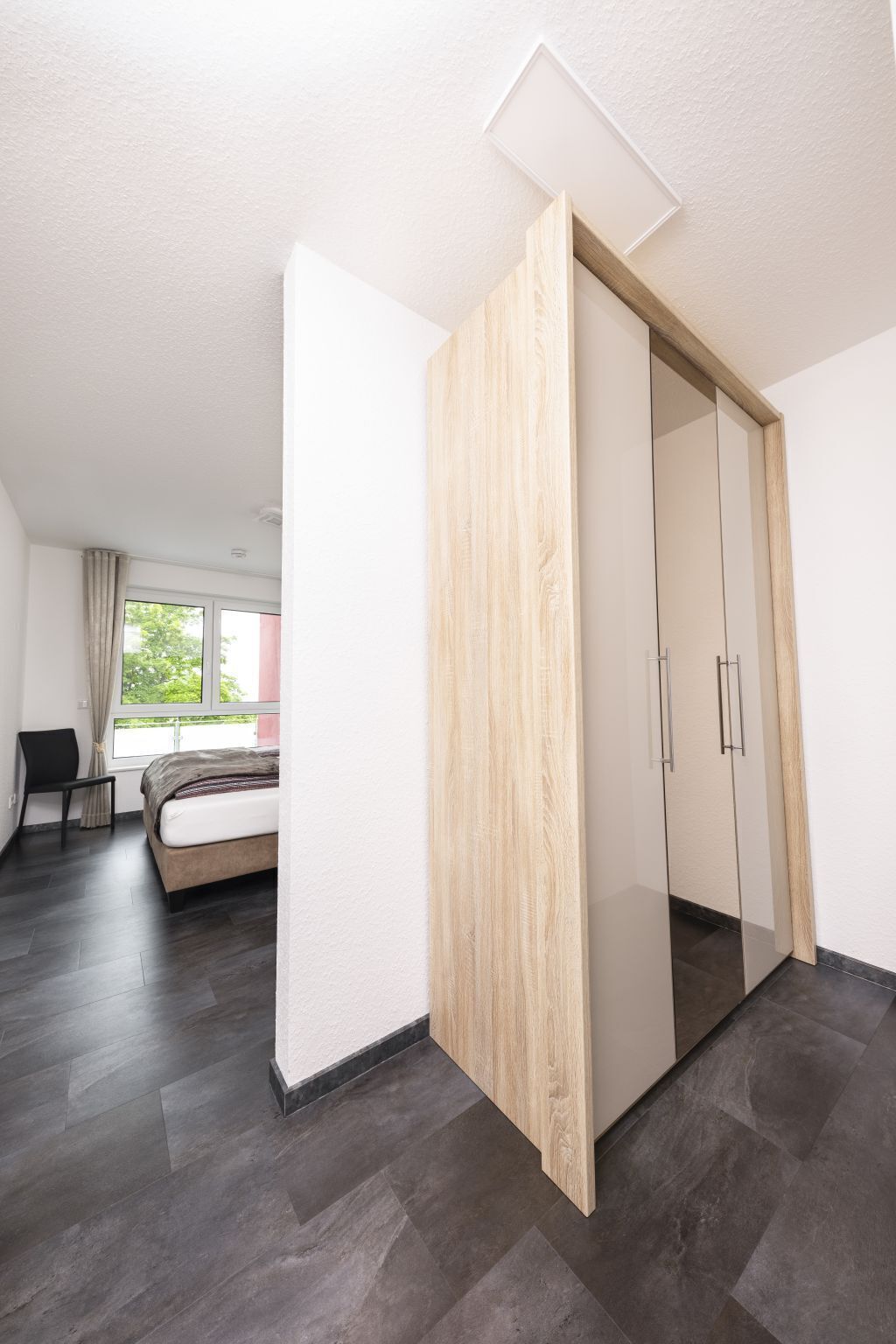 A modern room with a bed, a chair, a wardrobe, and a window.