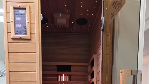 Uma sauna com paredes de madeira e porta de vidro, com painel de controle e porta-toalhas.