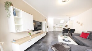 Uma sala de estar moderna com televisão de tela plana, sofá, área de jantar e cozinha ao fundo.