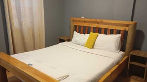 Una cama de madera con colchón blanco y almohada amarilla, dos mesitas de noche y un cabecero de madera.