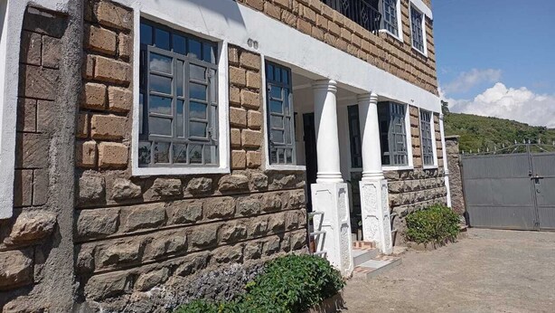Un edificio de piedra de dos plantas, con balcón, ventanas grandes y entrada protegida por una reja.