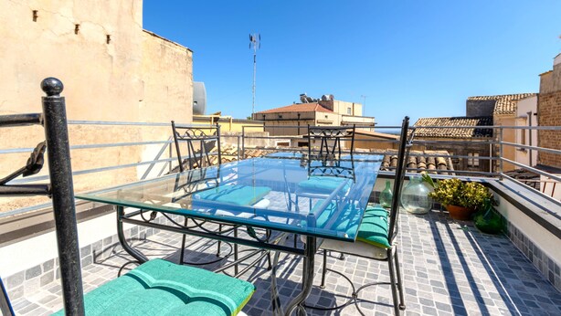A rooftop terrace with a glass table, chairs, and a potted plant. - Casa Vico Ferruccio 24 (Noto (SR))