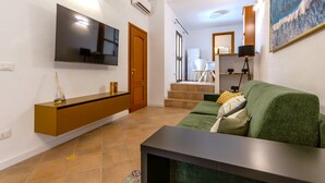 A modern living room with a flat-screen TV, a wooden entertainment unit, a green sofa, and a staircase leading to an upper level. - Casa Vico Ferruccio 24 (Noto (SR))