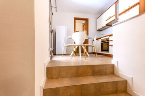 A staircase leading to a dining area with a white table and chairs, a kitchen with cabinets and a stove, and a door in the background.