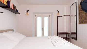 Una camera da letto con un letto, un comodino con asciugamani, una libreria, un armadio e uno specchio.