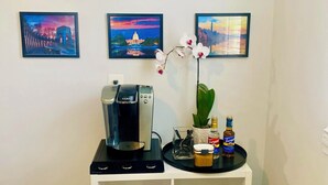 Ein Kaffee-Bereich mit einer Keurig-Maschine, einer Serviertafel mit Beilagen und einer Topfpflanze.