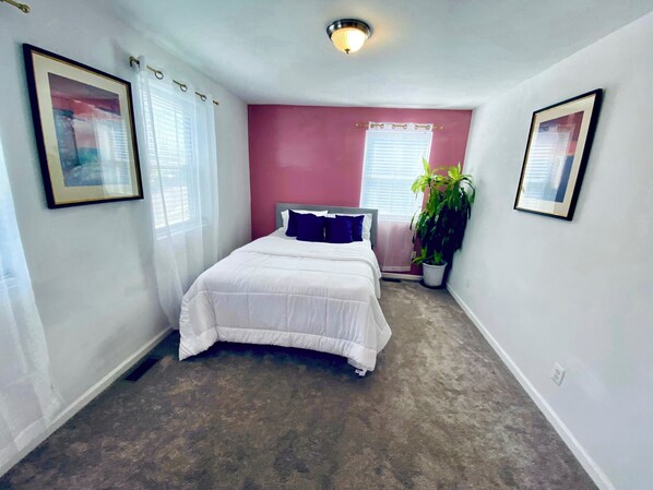 Une chambre à coucher avec un lit, une plante en pot et deux tableaux encadrés accrochés aux murs.