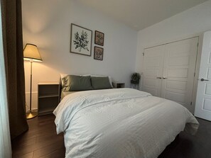 A bedroom with a bed, a nightstand, a lamp, a door, and wall art.