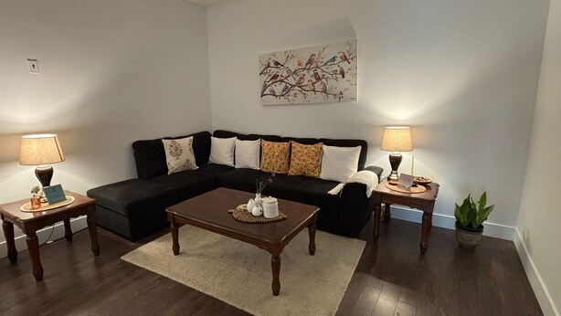 Ein Wohnzimmer mit einer schwarzen Couch, zwei Beistelltischen mit Lampen, einem Couchtisch und einem Gemälde an der Wand.