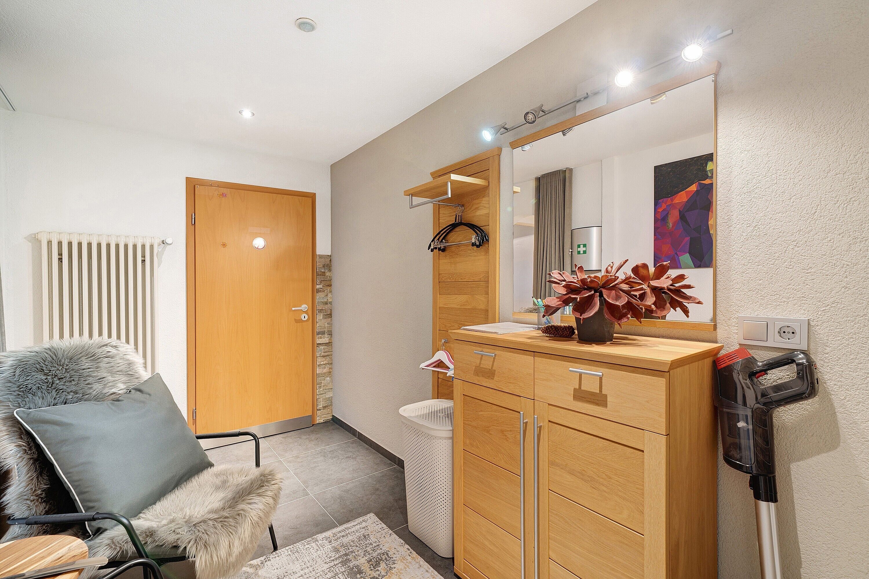 Un baño moderno con tocador de madera, un espejo, un radiador, una silla con una manta de piel y una aspiradora.