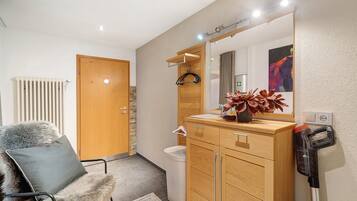 Un baño moderno con tocador de madera, un espejo, un radiador, una silla con una manta de piel y una aspiradora.