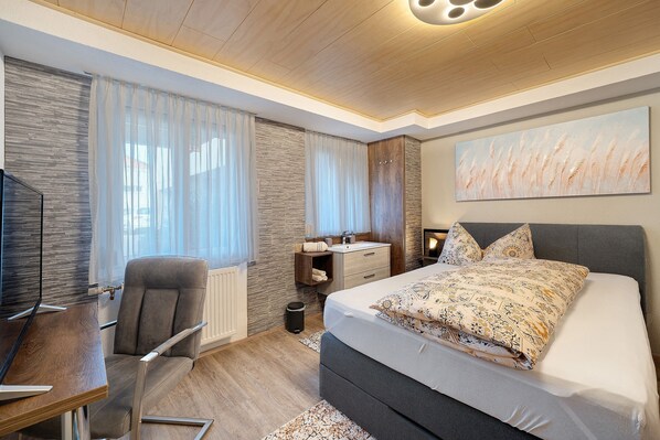 Une chambre moderne avec un lit, un bureau, une chaise et une grande fenêtre avec des rideaux.