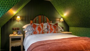 A bedroom with a sloped ceiling, a bed with a red quilt, two bedside lamps, and a nightstand with a clock. - Luxury rural escape in peaceful Aberdeenshire (Alford)