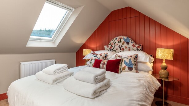 A bedroom with a sloped ceiling, a skylight, a bed with white linens and decorative pillows, two bedside lamps, and a radiator. - Greenstyle  - Countryside retreat with castle views (Kildrummy)