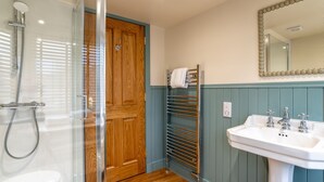 A bathroom with a glass shower enclosure, wooden door, towel rack, sink with two faucets, and a mirror with a decorative frame. - Greenstyle  - Countryside retreat with castle views (Kildrummy)