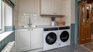A laundry room with two front-loading washing machines, a sink, and a cabinet above. - Greenstyle  - Countryside retreat with castle views (Kildrummy)