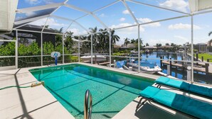 Una piscina con zona cubierta, sillas de descanso y vistas a un puerto deportivo con barcos.