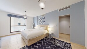 A modern hotel room with a large bed, bedside tables, a window with blinds, and a door.