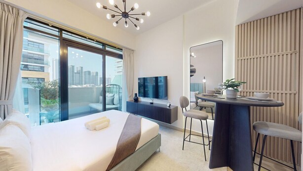 A modern hotel room with a large bed, a desk with a chair, a TV, and a city view. - Peaceful Studio l Spacious & Bright l Meydan (Meydan)