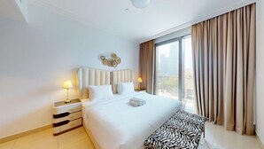 Habitación de hotel con una cama grande, una mesita de noche con lámpara y vistas a la ciudad desde la ventana.
