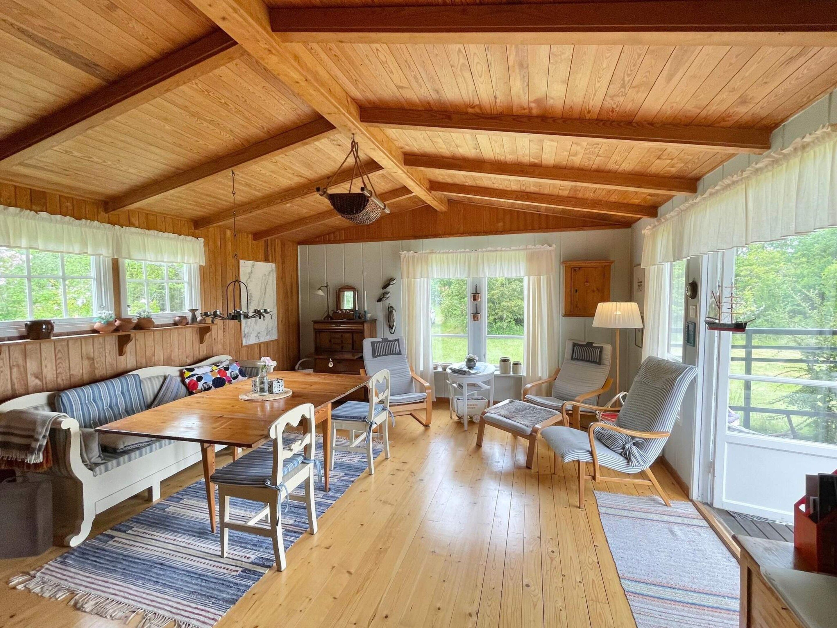 Une pièce chaleureuse avec un plafond en bois, une table à manger avec des chaises, un canapé et une fenêtre avec des rideaux.