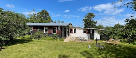 Eingeschossiges Haus mit Veranda, kleiner Terrasse und Rasen.