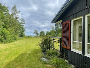 Une maison avec une cour verdoyante, une terrasse en bois et une vue sur la mer.