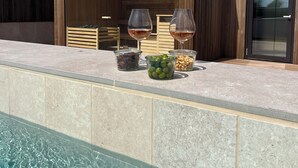 A modern outdoor pool area with a wooden deck, two wine glasses, and bowls of snacks. - Hotel de Ville (Gilleleje)