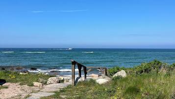 Kystlandskab med en trækonstruktion, klippefyldt terræn og havet.