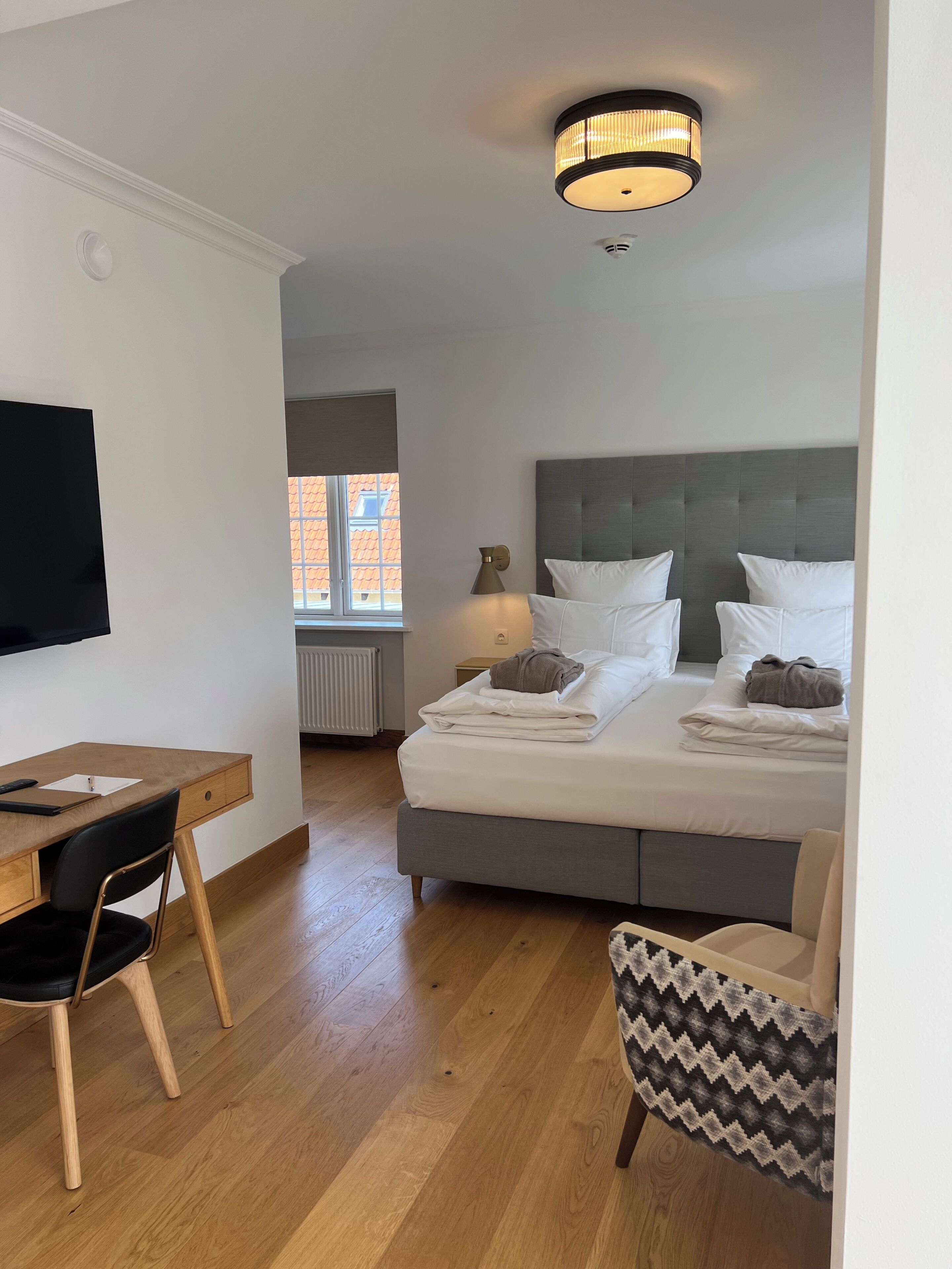 A hotel room with a bed, a desk, a chair, a television, and a window.