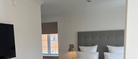 A hotel room with a bed, a desk, a chair, a television, and a window.
