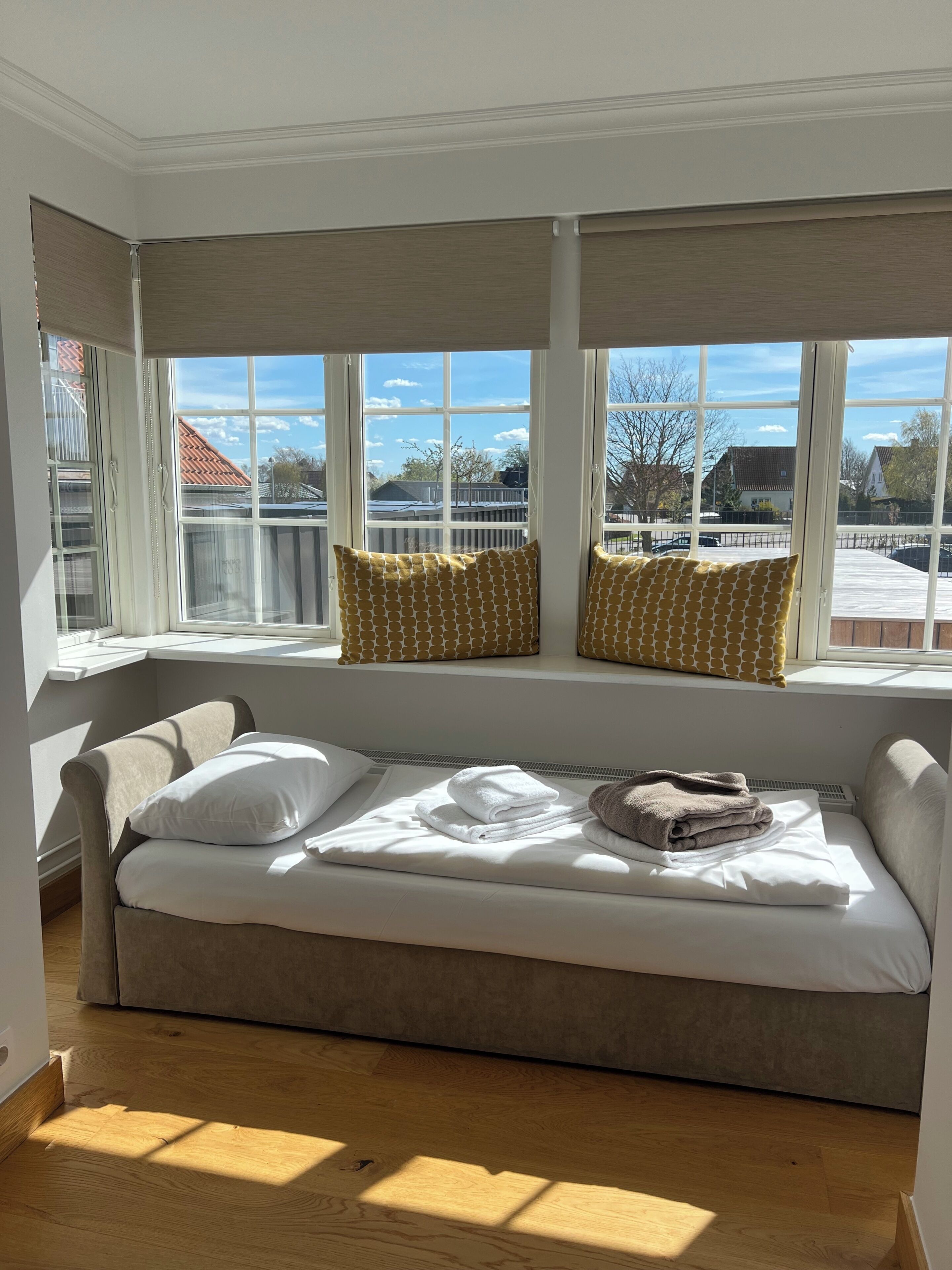 Una habitación con una cama, una ventana con persianas y vistas a edificios.