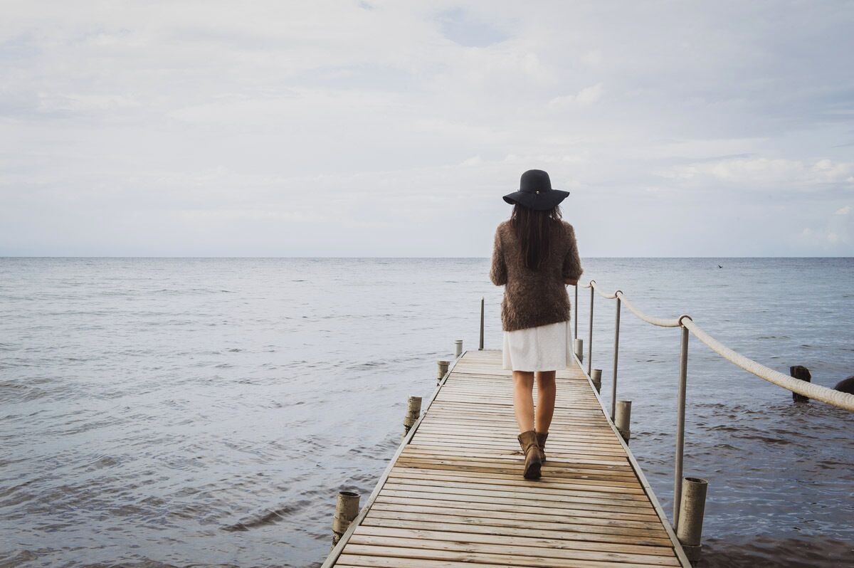 Une personne marchant sur une jetée en bois, en direction de la mer.