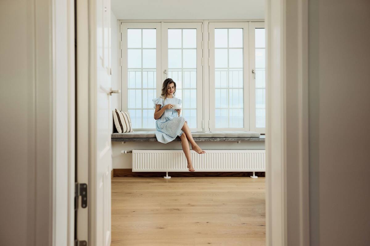 Eine Person sitzt auf einer Bank neben einem Fenster mit Blick auf die Landschaft.