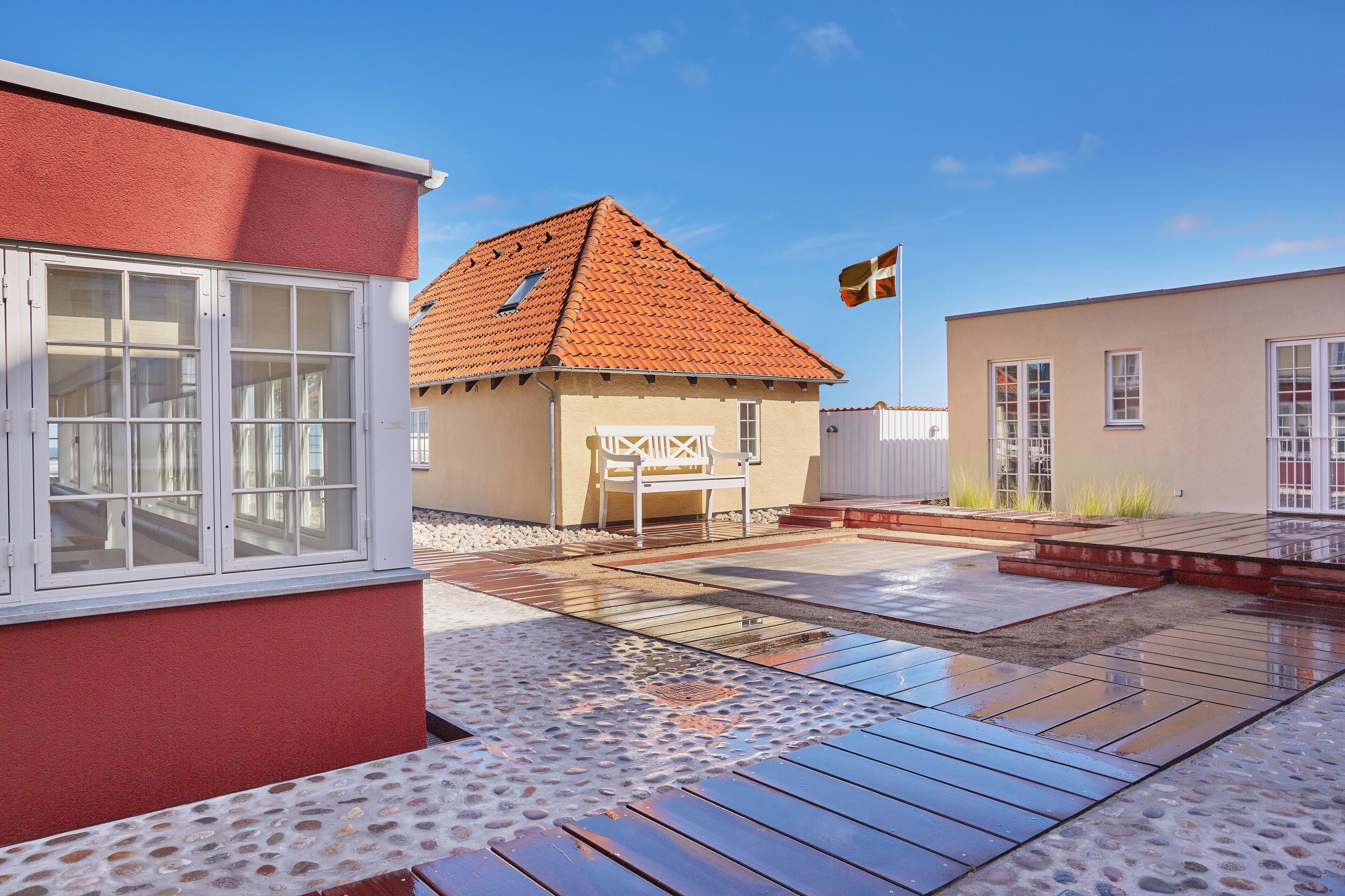 En boligejendom med røde facader, et tegltag og en terrasse med træterrasse og stensætning.